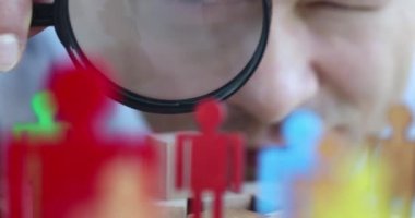 Man manager looking through magnifying glass at figures of men closeup 4k movie slow motion. Employee search concept