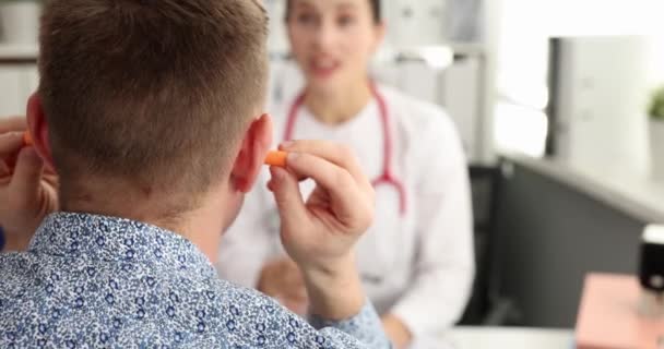 在诊所的4K电影中 男病人在与医生交谈时 把耳塞插入他的耳朵 为什么病人不遵循医生的建议概念 — 图库视频影像