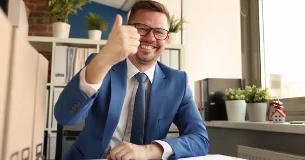 眼鏡をかけたビジネスマンがテーブルに座り 親指を立てて4K動画を見せます 成功したビジネスコンセプト — ストック動画