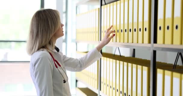 女性医師は棚から黄色のフォルダを取ります 医療文書を探しているセラピスト — ストック動画