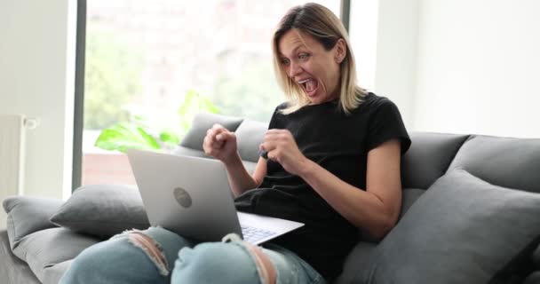 庆祝胜利的快乐女性获胜者坐在沙发上 用笔记本电脑庆祝胜利 女孩在网上赢了很兴奋有了新的工作机会 — 图库视频影像