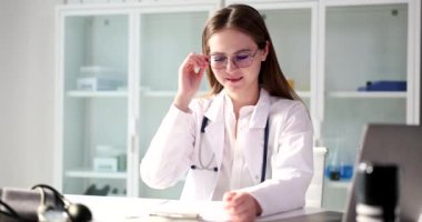Yorgun kadın doktor klinikteki iş yerinde gözlüğünü çıkarıyor. Fazla mesai ve fazla mesai yapan doktorlar.