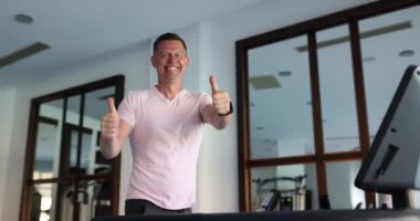 Genç adam modern spor salonunda koşu bandında koşuyor ve iyi niyet gösterisi yapıyor. Mutluluk duyguları, spor yapma sevinci.
