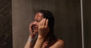 Genç bir kadın ağır çekimde duş alıyor. Duşun altındaki güzel kız başı ve damlaların ve yüzdeki su akışının keyfini çıkar.