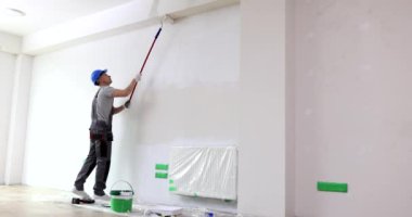 Adam tavanı beyaz odada silindirle boyuyor. Duvar ve tavan onarımı ve boyaması