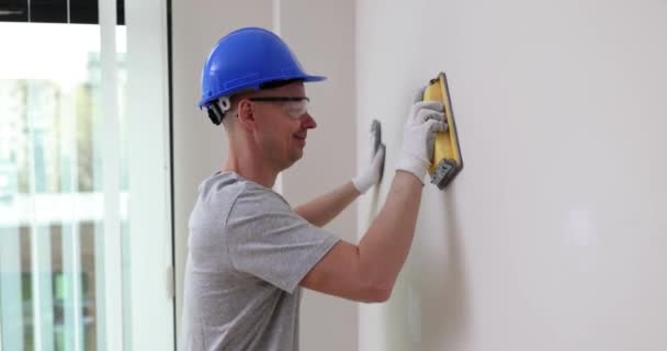 労働者は部屋の中でサンドペーパーの壁をレベリングしている 石膏で壁をレベリングし 詳細な指示 — ストック動画