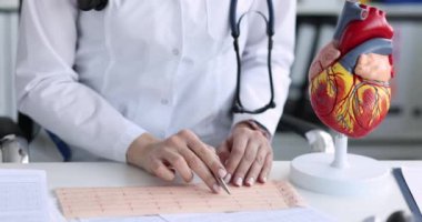 Doktor kardiyolog kalp filmlerinin yavaş çekim modelinin arka planındaki elektrokardiyogramı inceliyor. Ritim ve iletkenlik bozuklukları ECG teşhisi