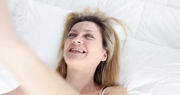 Yatakta Uzanmış Neşeli Bir Kadın Akıllı Telefon Kamerasına Gülümsüyor Selfie — Stok video