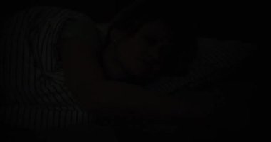A woman wakes up in bed at night from a thunderstorm and lightning, close-up. Light from an electric charge outside the window