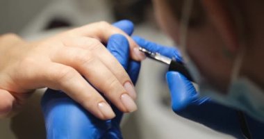 Manicurist applies transparent gel on womans nails, close-up. Strengthening of the nail plate, cosmetic procedure