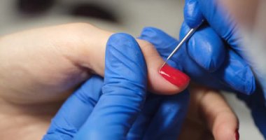 Manicurist makes a manicure with red varnish, hands close-up. Gel polish under the cuticle, training