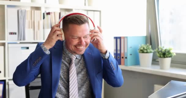 幸せなビジネスマンは職場に座っている間にヘッドフォンをして楽しく踊ります 仕事のコンセプトにおけるポジティブな気分と感情 — ストック動画