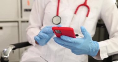Tıbbi eldivenli doktor klinikteki akıllı telefon ekranında yazı yazıyor. Doktorlar için tıbbi mobil uygulama