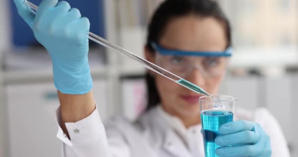 Woman scientist chemist dripping blue liquid from pipette into flask in laboratory 4k movie. Pharmaceutical industry concept
