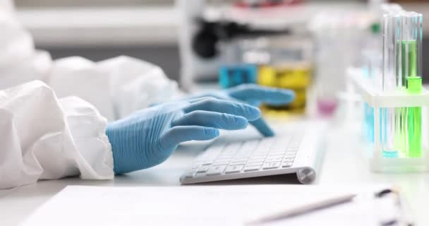 在实验室4K胶片的试管附近 身穿防护服和手套在键盘上打字的科学家化学家 开发免疫联盟概念的疫苗19 — 图库视频影像