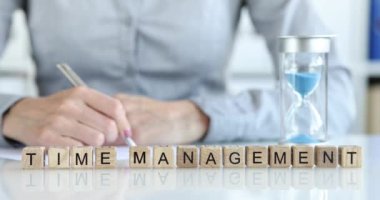 A woman writes at the table, on wooden cubes the inscription time management, close-up, slow motion. Efficient office work