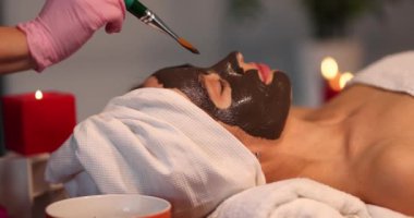 The cosmetologist applies a mask with a brush on the face of a lying woman, close-up. Chocolate face mask