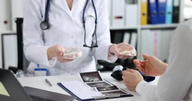 A plastic surgeon shows a woman breast implants. Breast augmentation, preparation for surgery