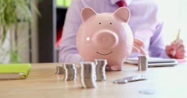 There is a pink piggy bank and coins on the table in the office, close-up. Distribution of profits, income from the deposit