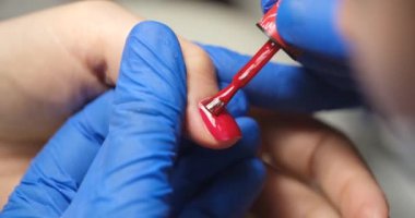 Manicurist applies red lacquer on a womans finger, close-up. Manicure correction, cosmetic procedure