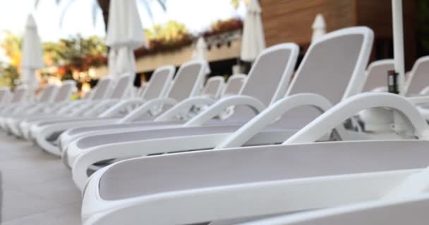 阳光明媚的日子 清澈的白色塑料日光浴者排成一排站在海滩或游泳池边 康乐区和座位区 — 图库视频影像