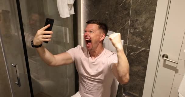Překvapený Šťastný Držení Telefonu Při Pohledu Mobilní Smartphone Sedí Záchodě — Stock video