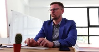 Yorgun iş adamı burun köprüsüne masaj yapar, iş yerinde gözlüğünü çıkarır. İşadamı masasında oturan yorgun gözleri hissediyor