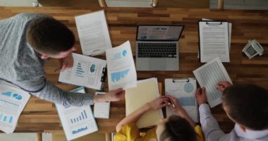 Çalışanlardan oluşan bir ekip dizüstü bilgisayarın etrafında yeni iş planlarını tartışıyor. İstatistik belgeleriyle büyük ahşap masadaki meslektaşlar ve yavaş çekim raporları