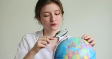 Düşünceli genç kadın büyüteçle Dünya 'yı ziyaret edecek popüler ülkeleri dikkatle arıyor. Beyaz gömlekli bayan dünyayı dolaşmayı hayal ediyor.