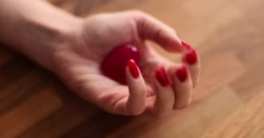 Kırmızı tırnaklı kadın eli küçük bir kalp oyuncağı figürü gösteriyor. Ahşap yüzeyde zarif bir kadın avucunda aşkın sembolü. Ağır çekimde dikkat et ve destekle