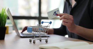 Kadın, alışveriş arabasıyla masada oturarak satın almak için kart detaylarını giriyor. Çevrimiçi sistem yavaş çekim yoluyla modern e-ödeme kavramı