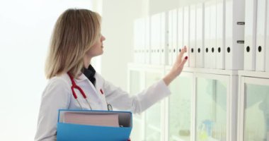 Odaklanmış kadın doktor, hasta hakkındaki verileri içeren gerekli belgeler için yüzük klasörlerine bakıyor. Hafif çekimde organize dizin yapısı ve arşivi
