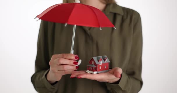 女性は建物を保護するために傘の下で手のひらに小さなおもちゃの家を保持します 不動産屋は安全性を保証します 保険契約の概念で家を守る — ストック動画