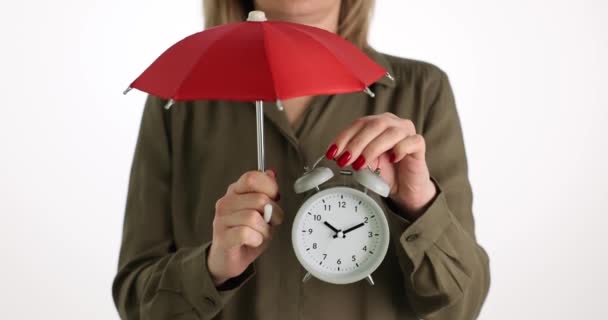 女人带着老式的白色闹钟和红色雨伞 手握浅色工作室背景 时间管理和组织概念 — 图库视频影像