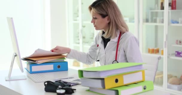 Kobieta Przeszukuje Dokumenty Pacjentów Siedzących Przy Stole Folderami Klinice Zmęczona — Wideo stockowe