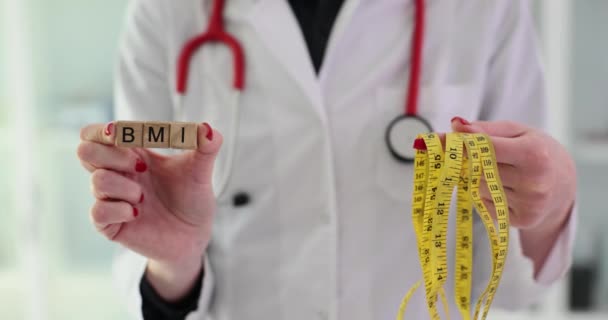 医師は木のブロックからBmiという単語を保持し 診療所のオフィスに立って測定するテープを測定します パラメータを測定するためのボディマス指数及び装置 — ストック動画
