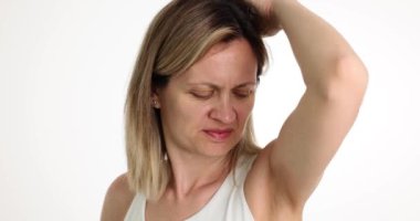 Beyaz gömlekli genç bir kadın arka planda, koltukaltını kokluyor. Bayan kötü vücut kokusundan ürkmüş. Kötü ter kokusu. Kronik hastalıklar veya kötü kalite deodorant