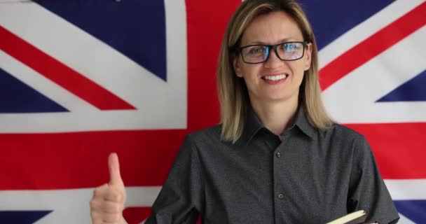 戴眼镜的年轻妇女表现出尊重语言的大拇指向上的姿态 英语老师高举英国国旗 鼓励学生学习 — 图库视频影像