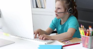 Kulaklıklı küçük bir kız bilgisayar klavyesinde yazı yazıyor ve 4K ekran filmine bakıyor. Çocuk konsepti için eğitici çevrimiçi kurslar