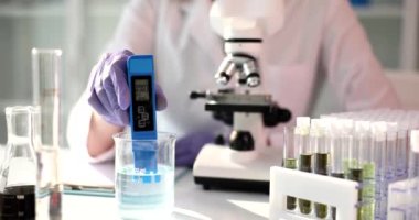 Lastik eldivenli bir laboratuvar uzmanı pH seviyesinde şeffaf kimyasal sıvıyı ölçer. Mikroskop ve test tüpleriyle sterilize edilebilir. PH ölçer