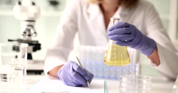 女性实验室工作人员拿着装有病人尿液检测结果的瓶 写下研究结果 无菌诊所的实验室工作人员把数据填入医疗空白 — 图库视频影像