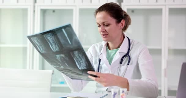 身穿白衣的年轻女医生在检查了病人脊柱的X光图像后 写下了治疗处方 后背严重受伤 健康危害伤害 — 图库视频影像