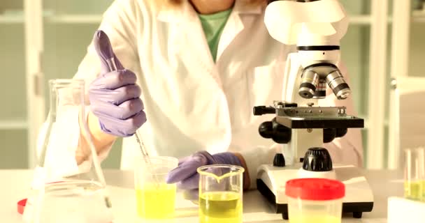 実験室の女性科学者は ピペットで分析するために瓶から患者の尿のサンプルを取り 顕微鏡ステージに注ぎます 現代クリニックの医療研究員 — ストック動画
