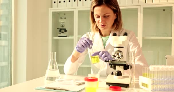 女性研究室の労働者は 試験管に注ぐ前に患者の尿サンプルを瓶に撹拌する 濃縮科学者は研究のための液体を準備する 研究室での医学分析 — ストック動画
