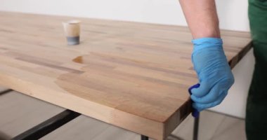 Adam cilalanmış ofis masası yüzeyini cila beziyle cilalıyor. Kauçuk eldivenli marangoz, ahşap işleri yavaş çekimde parlatma kavramı.