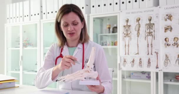 現代のクリニックで患者に手の骨格を示す医師療法士 女性の専門整形外科医は 骨や関節への傷害の影響を説明しますスローモーション — ストック動画
