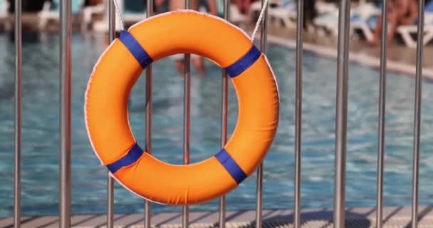 スイミングゲストを背景にホテルの子供プールの近くのフェンスにかかっているオレンジライフブイ ホテルの水泳安全対策 — ストック動画