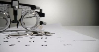 Optometric glasses for measuring visual acuity lie on paper Snellen chart in clinic office. Medical equipment for checking eyesight waits for client