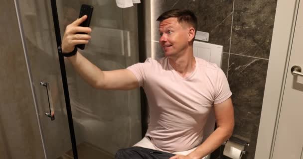 Male Person Takes Funny Selfie Sitting Toilet Bowl Light Bathroom — стоковое видео
