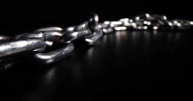 Massive silver chain links made of steel lies on black surface leaving bright reflection. Galvanized massive hard chains for different purposes put in dark studio